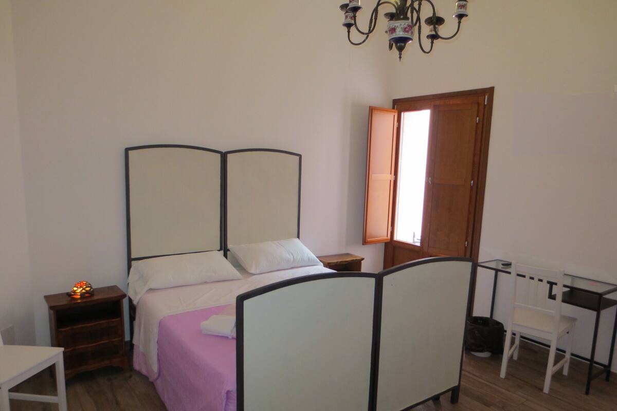 A bedroom with a bed, bedside table, chair, and a desk.