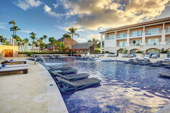 A resort pool with lounge chairs, palm trees, and a building with multiple balconies. - Royalton Hideaway Punta Cana, An Autograph Collection All-Inclusive Resort & Casino – Adults Only (Punta Cana)