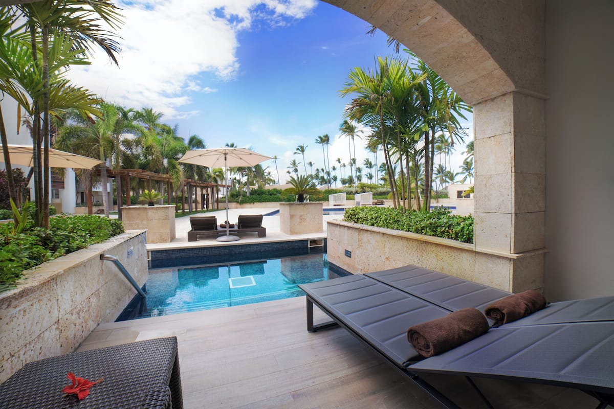 A pool area with lounge chairs, a small pool, palm trees, and a clear sky.
