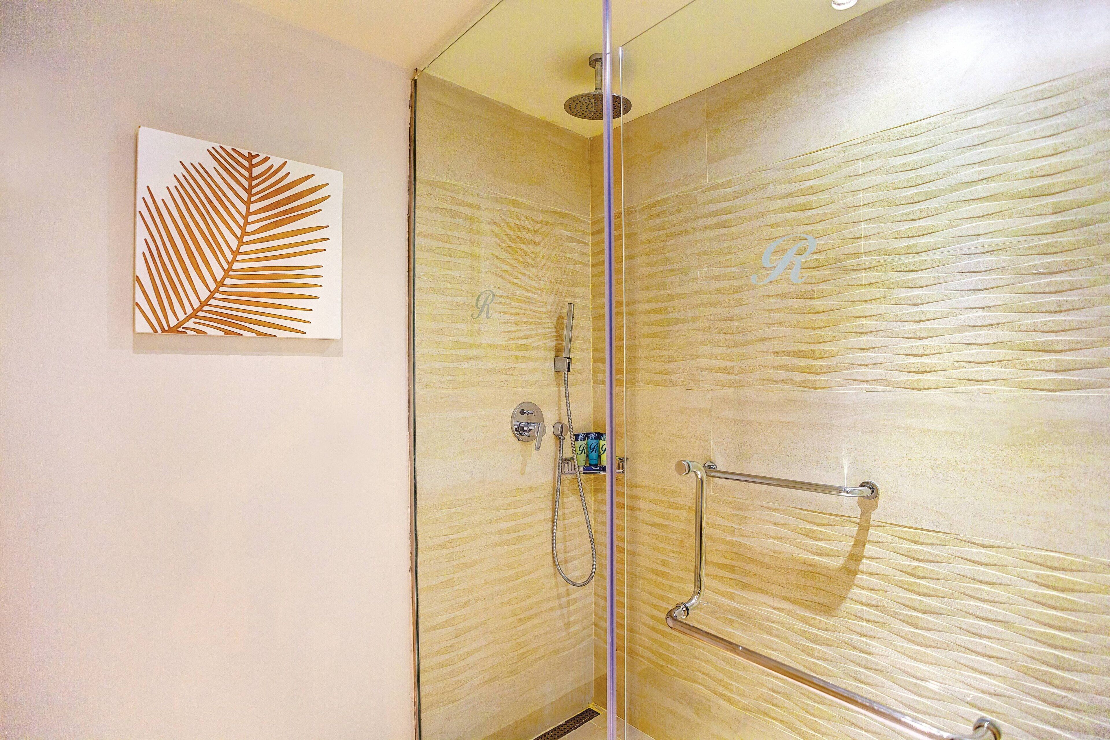 A glass-enclosed shower with a textured wall, a handrail, and a decorative leaf artwork on the wall.