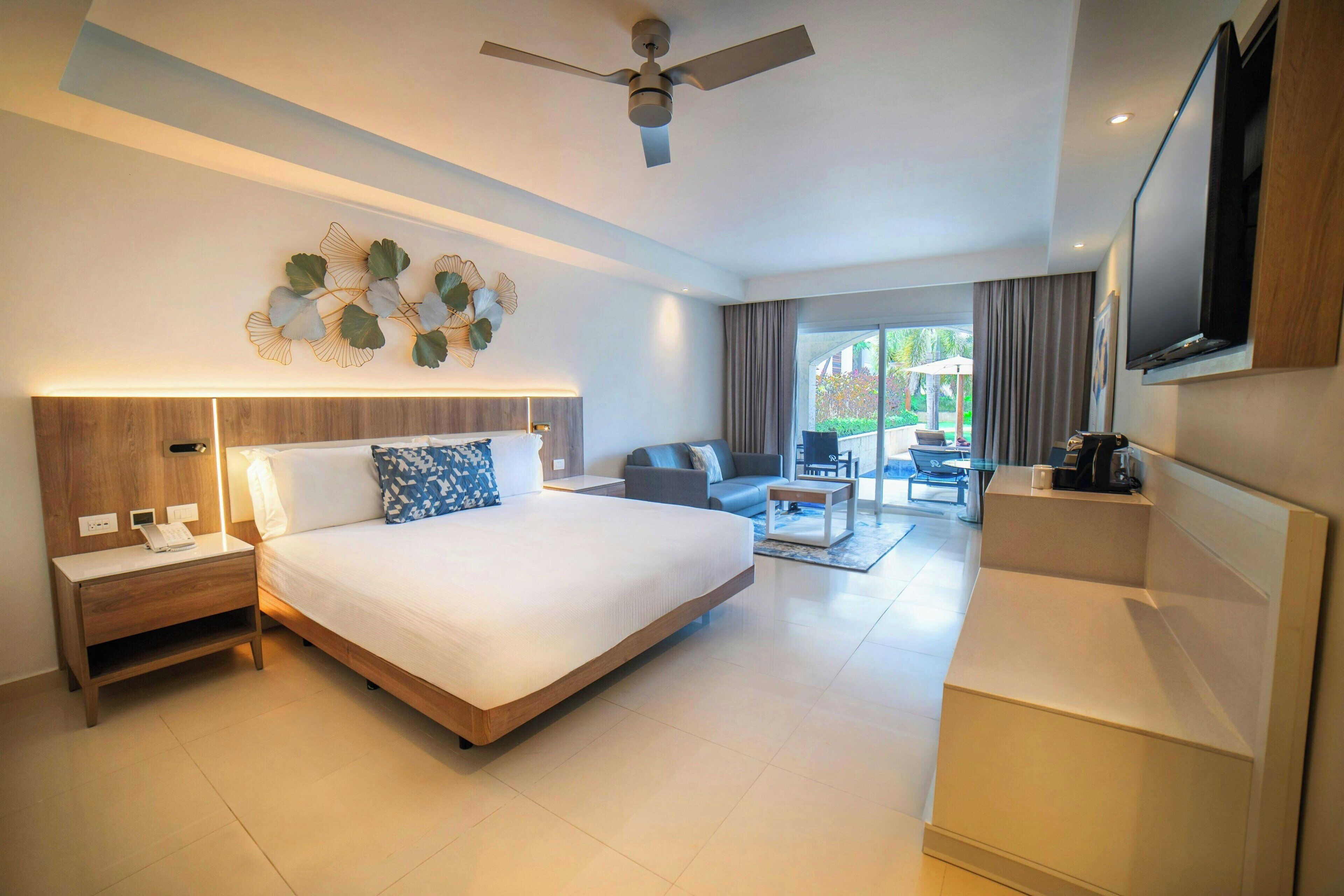 A modern hotel room with a large bed, a desk, a TV, and a balcony with a view.