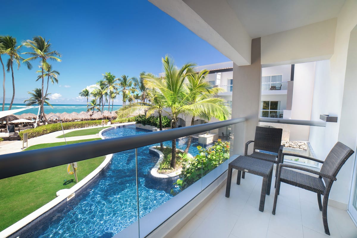 A balcony with a view of a swimming pool, palm trees, and a beach.
