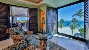 Una habitación con un gran ventanal que da a un balcón, un sofá estampado, una mesa de centro de vidrio con una escultura de caballo, y vista a la playa.