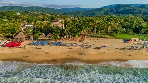 Una playa con sombrillas, gente, palmeras y edificios al fondo.