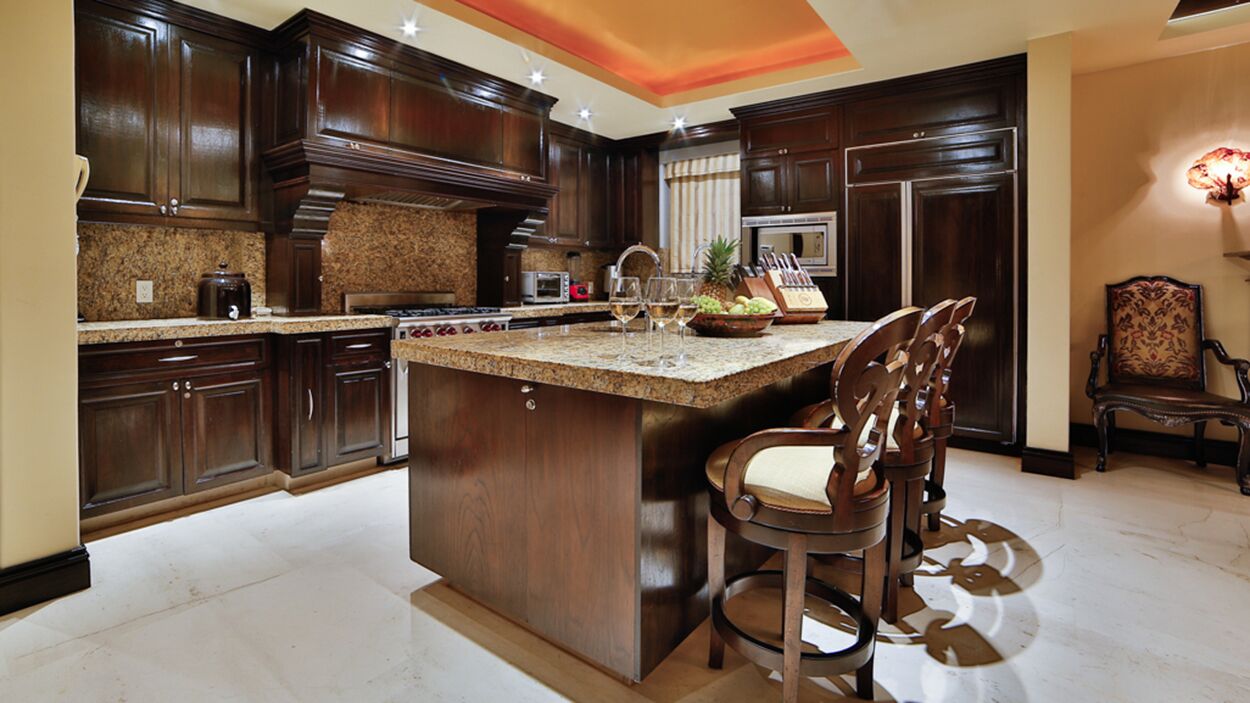 A spacious kitchen with dark wood cabinets, granite countertops, and a central island with bar stools.