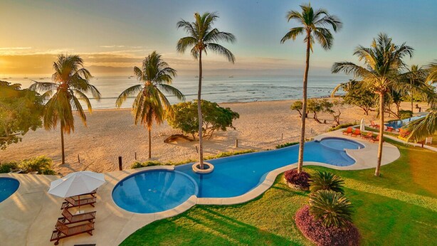 Zona de piscina con palmeras y vista al mar.