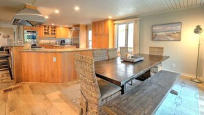 A spacious kitchen with wooden cabinets, a central island, and a dining area with a large table and wicker chairs. - Relax in your Private Oceanfront Paradise. Spacious Luxury, Awe-Inspiring Views. (Hilton Head Island)
