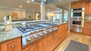 Une cuisine équipée d’une grande cuisinière à gaz, d’appareils électroménagers en acier inoxydable, de meubles en bois et d’un plan de travail en granit.