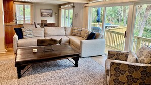 A spacious living room with a large sectional sofa, a coffee table, and a patterned rug. There is a wooden deck visible through the glass doors. - Relax in your Private Oceanfront Paradise. Spacious Luxury, Awe-Inspiring Views. (Hilton Head Island)