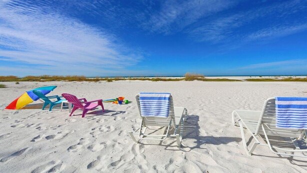A beach with two white lounge chairs with blue-striped towels, a colorful beach umbrella, and a pink beach chair. - #1 SIESTA KEY Beach Glass House w/supplies
 PRICE Breaks w/ 3 payments ! (Siesta Key)