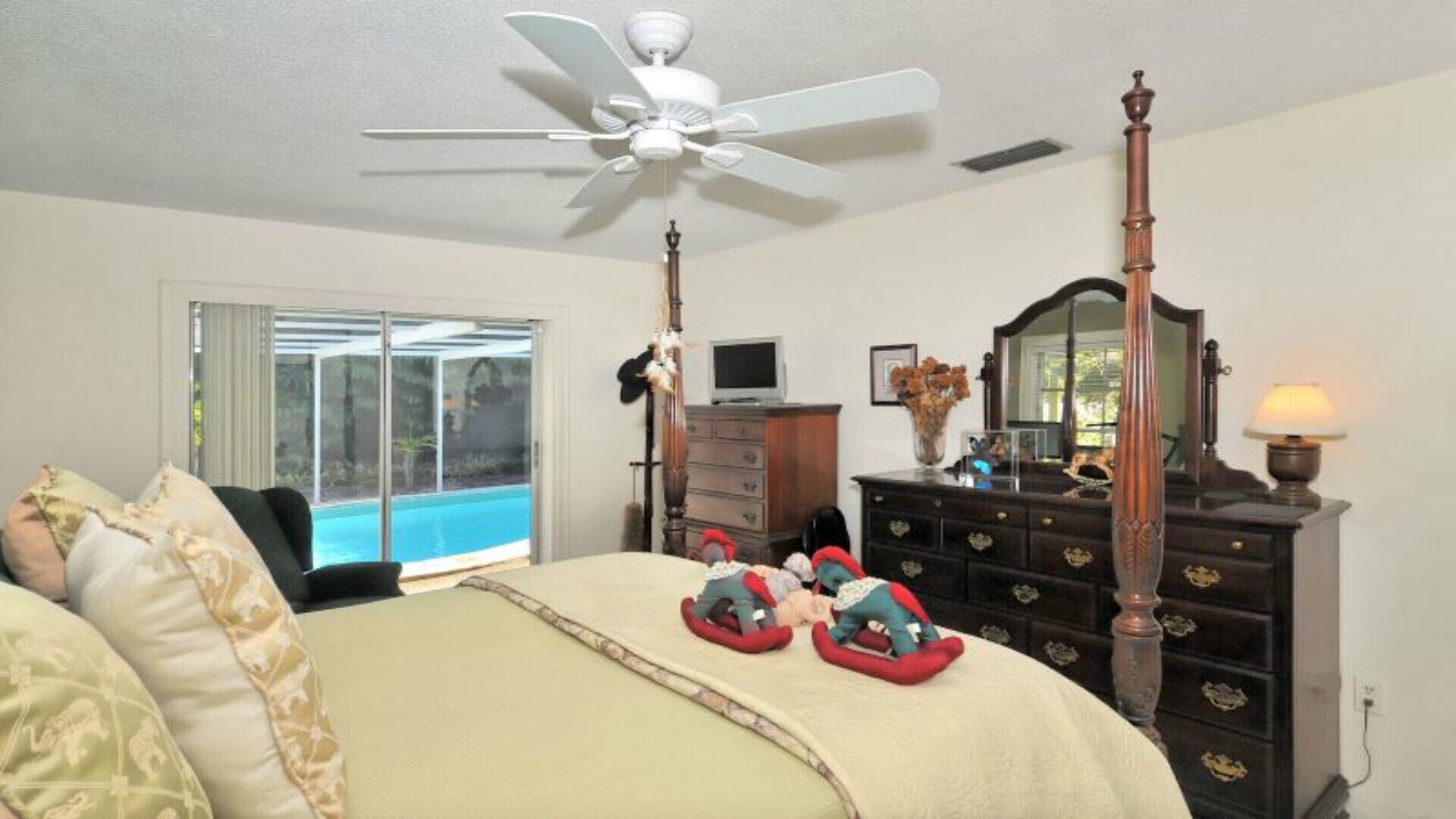 A bedroom with a bed, a dresser, a mirror, a ceiling fan, and a view of a swimming pool.