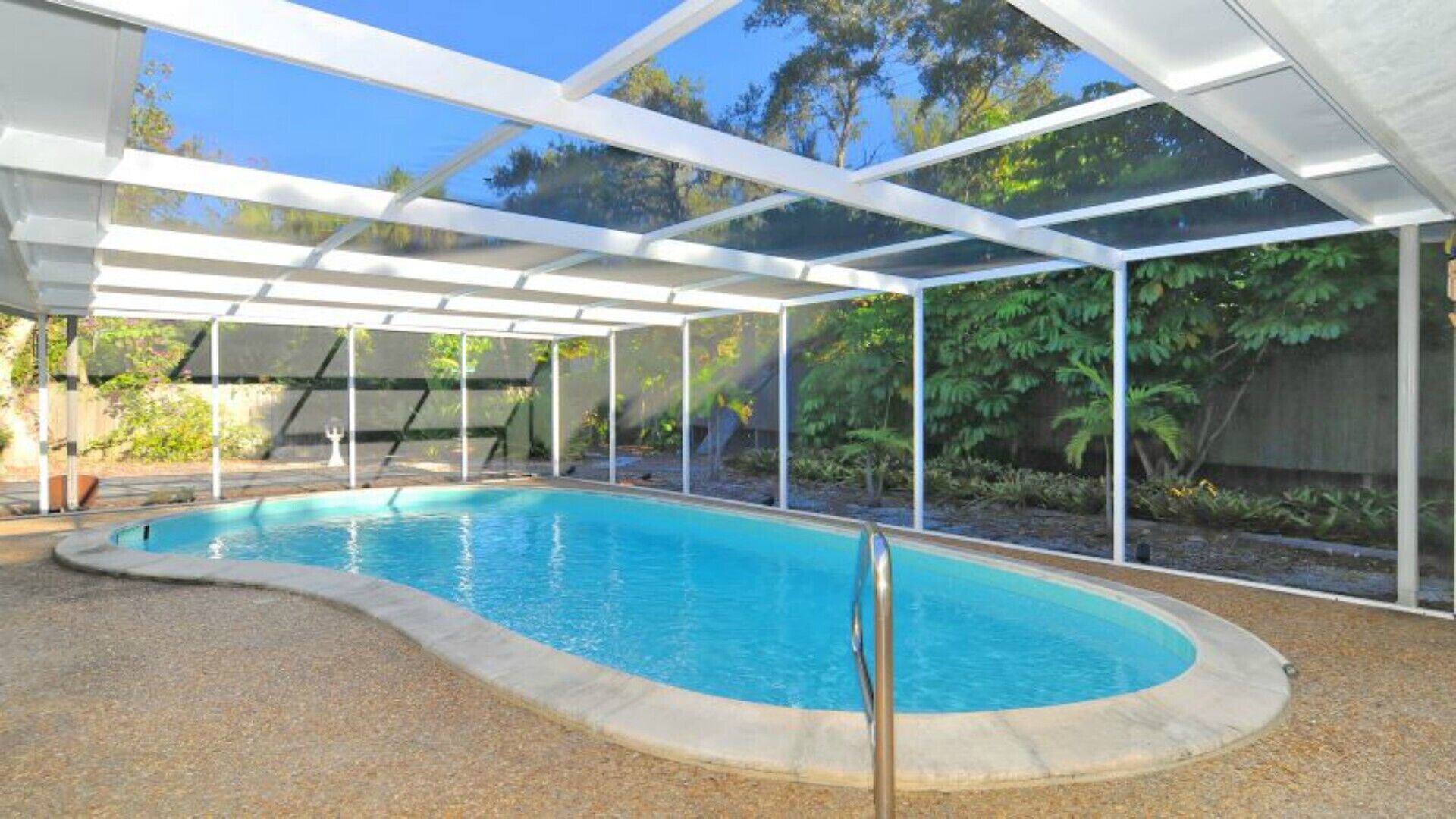 A covered swimming pool with a clear view of the surrounding garden and trees.