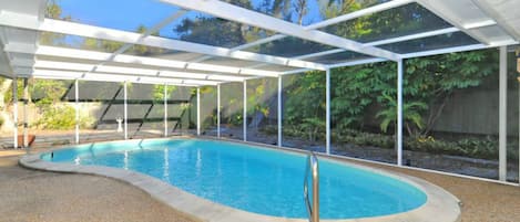 A covered swimming pool with a clear view of the surrounding garden and trees.