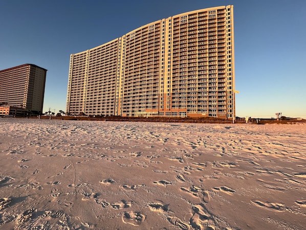 Un grand hôtel à plusieurs étages, doté de balcons, situé sur une plage de sable.