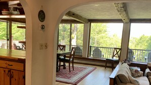 A spacious living area with a wooden floor, a sofa, a dining table with chairs, and large windows offering a view of trees. - Unique & charming home with stunning view of Mt Washington. Pet friendly. (Jackson)