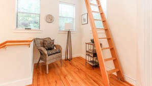 A room with wooden flooring, a wicker chair with patterned cushions, a wooden ladder, and two windows with blinds. - Downtown oasis, walking distance to Capitol, UT, Zilker Park, music venues (Austin)