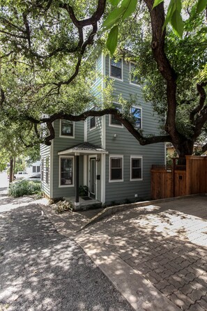A two-story house with a porch, a wooden fence, and a large tree providing shade. - Downtown oasis, walking distance to Capitol, UT, Zilker Park, music venues (Austin)