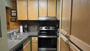 Une cuisine de taille réduite, dotée de meubles en bois, d’une cuisinière en acier inoxydable et d’un lave-vaisselle.