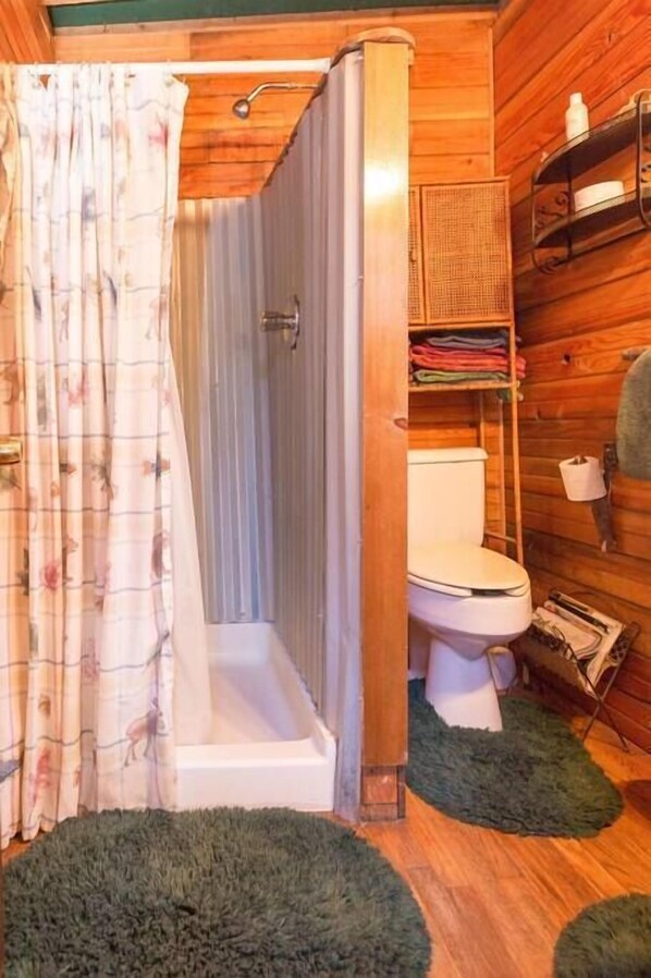 A wooden cabin bathroom with a shower, toilet, and shelves with towels.
