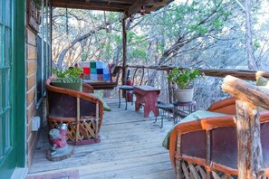 A wooden deck with rustic furniture, including a red stool and a bench, surrounded by trees.