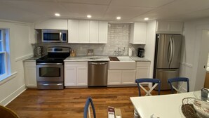 A modern kitchen with white cabinets, stainless steel appliances, and a wooden floor.