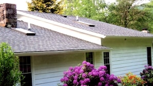 Une maison avec un toit à pignon, une cheminée et un porche à l’avant.