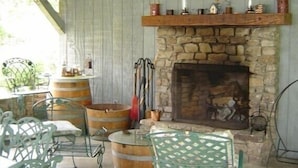 Un intérieur rustique avec une cheminée en pierre, des tonneaux en bois, des chaises en métal et une lanterne suspendue.