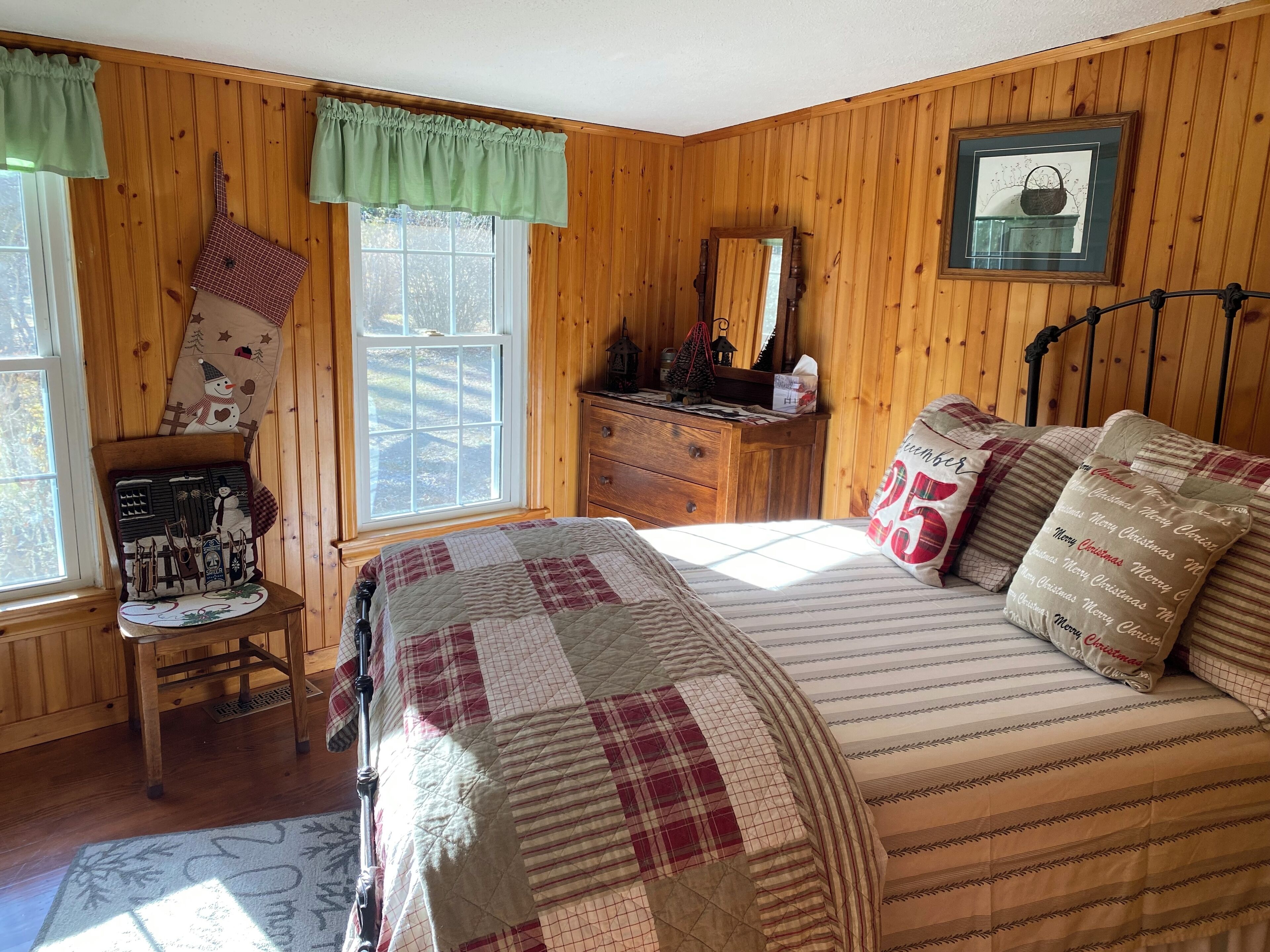 A cozy bedroom with a wooden paneled wall, a bed with striped bedding, a dresser, and a window with a view of the outdoors.