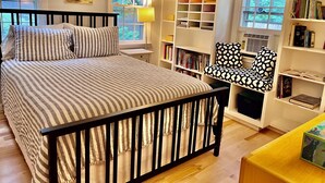 Ein Schlafzimmer mit Bett, Bücherregal, Sessel und Fenster.