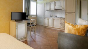 A compact hotel room with a bed, a desk with a TV, a chair, a kitchenette, and a sofa with patterned cushions. - Mimosa apartment in a farmhouse, with a park view (Scandiano)