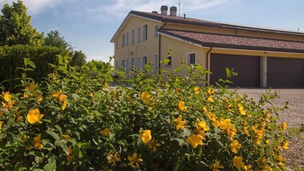 A yellow building with a tiled roof and a garage. - Mimosa apartment in a farmhouse, with a park view (Scandiano)
