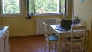 A small kitchen with a dining area, a window with curtains, a radiator, and a laptop on the table. - Mimosa apartment in a farmhouse, with a park view (Scandiano)