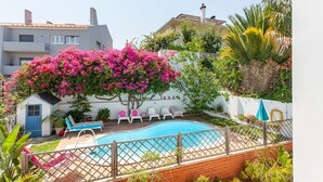 A swimming pool with lounge chairs, a small shed, and a tree with pink flowers. - Family Villa in LISBON,heated pool,elevator,parking,6 bedrooms,sleeps 14 (Lisboa)