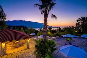 Relax and socialize in a serene outdoor space with lounge chairs and umbrellas, a bar, and a picturesque view of calm waters and distant mountains.