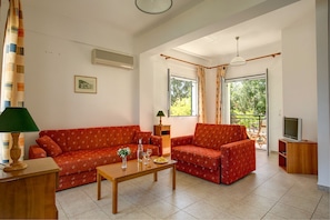 Relax in this inviting living room with a sofa, coffee table, and TV, surrounded by a window with a view and a cozy reading nook.