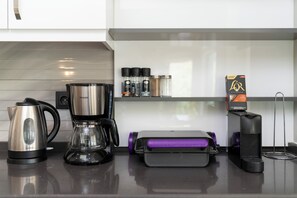 A kitchen counter with a coffee maker, a scale, a box of L'Or espresso capsules, and a set of spice containers.