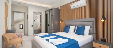 A modern hotel room with a large bed, a bedside table, a chair, and a built-in air conditioning unit.