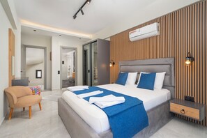 Een moderne hotelkamer met een groot bed, nachtkastje, stoel en een ingebouwde airconditioning.