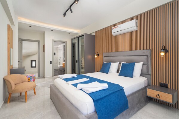 A modern hotel room with a large bed, a bedside table, a chair, and a built-in air conditioning unit.