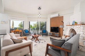 A modern living room with a fireplace, a flat-screen TV, and a dining area with outdoor seating.