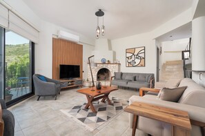Een moderne woonkamer met een open haard, een bank, een televisie en een balkon met uitzicht op groen.