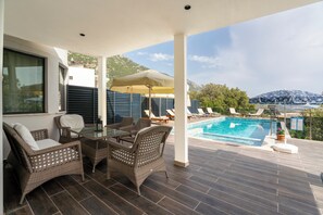 A covered outdoor area with a pool, wicker furniture, and a mountain view.