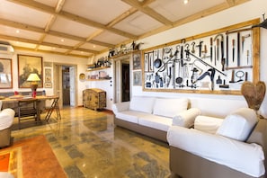 A spacious living room with a large white sofa, a wooden ceiling, and a wall decorated with various tools and kitchen utensils. - ClickSardegna Villa Girasoli with SPA and pool, Wifi, en-suite bathrooms (Olmedo)