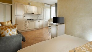 Una habitación de hotel pequeña con kitchenette, cama, televisión y sofá.