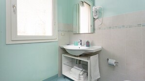 Un baño con lavamanos blanco, espejo, inodoro y ventana con persianas.