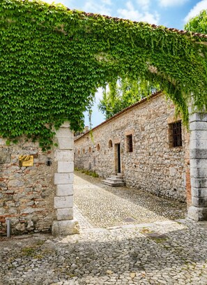A stone building with a cobblestone courtyard, arched doorways, and a covered walkway with greenery. - V. Ancient home with garden in a castle, near beach. Between Trieste and Venice (Strassoldo)