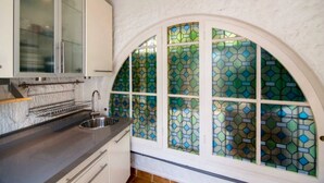 Una cocina de diseño moderno, con un lavamanos de acero inoxidable, armarios blancos y un ventanal de vidrio emplomado único.
