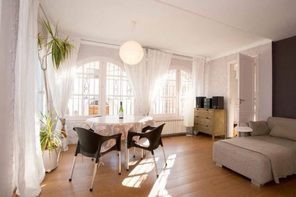A bright room with a dining table, chairs, a sofa, and a potted plant.