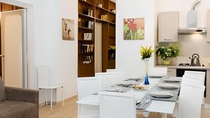 A modern living room with a dining area, white furniture, a bookshelf, and a kitchen area with a kettle. - GREGORY BIG FAMILY (Roma)