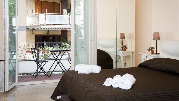 A hotel room with a bed, a desk, a chair, a small table, and a balcony with a table and chairs. - GREGORY BIG FAMILY (Roma)